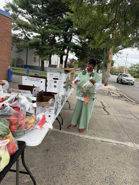 A neighbor picking up a bag of fresh vegetables at the distribution table