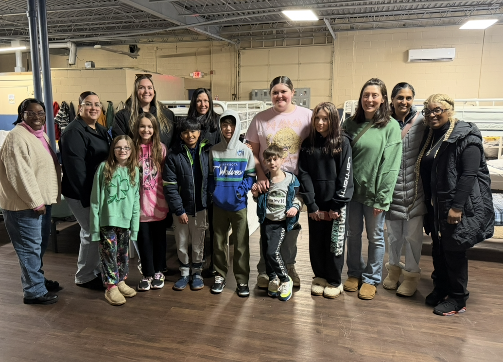Families, children and volunteers standing together in the shelter bunk room