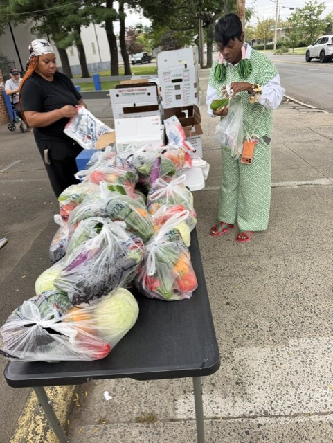 A volunteer and a neighbor sorting bags of produce at the outdoor distribution table